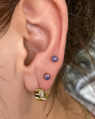 Stacked lobe piercings with opal studs in implant-grade titanium at Rebel Tattoos Gurgaon