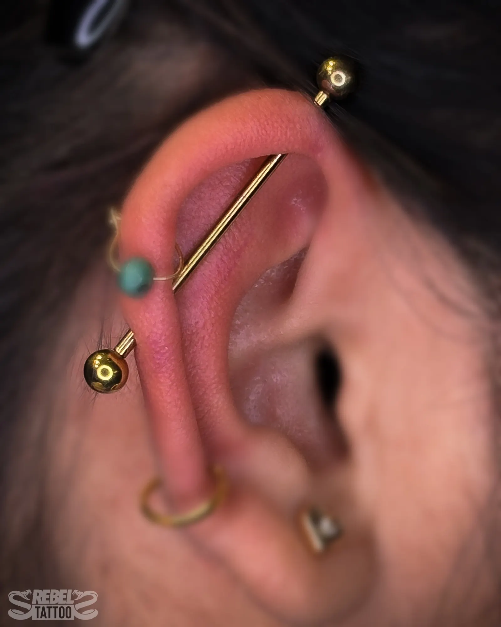 Industrial barbell piercing in anodised titanium with gold colour finish, across upper ear cartilage at Rebel Tattoos Gurgaon