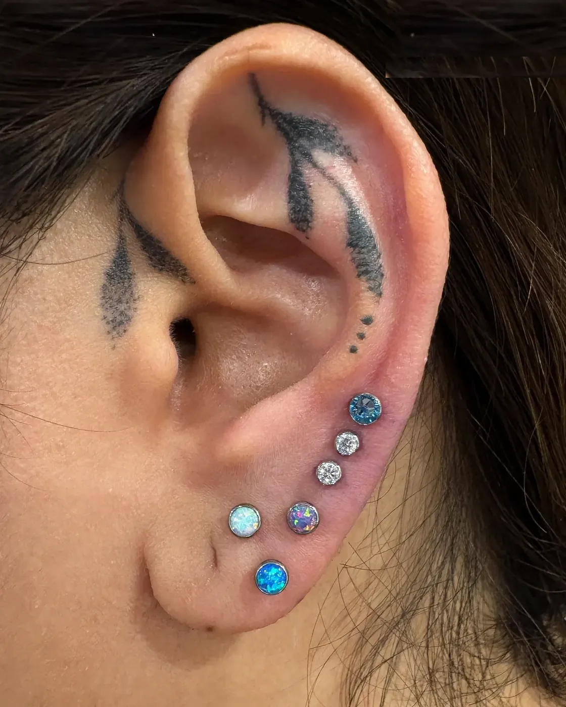 Curated lobe stack with opal and CZ studs in implant grade titanium, ear piercing at Rebel Tattoos Gurgaon